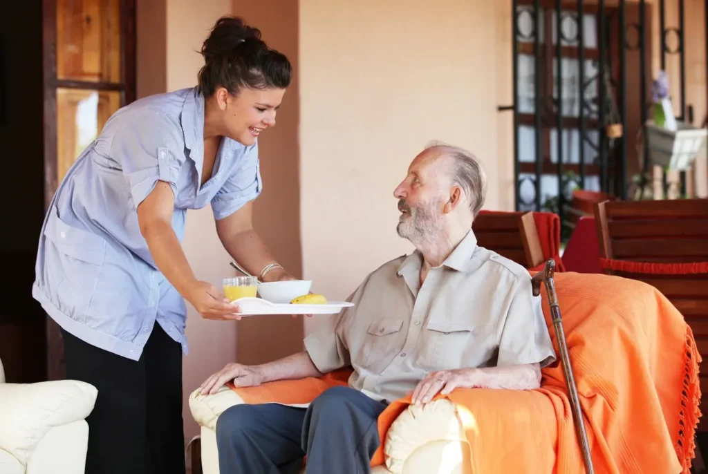 Empleada del hogar llevando la cena a anciano.