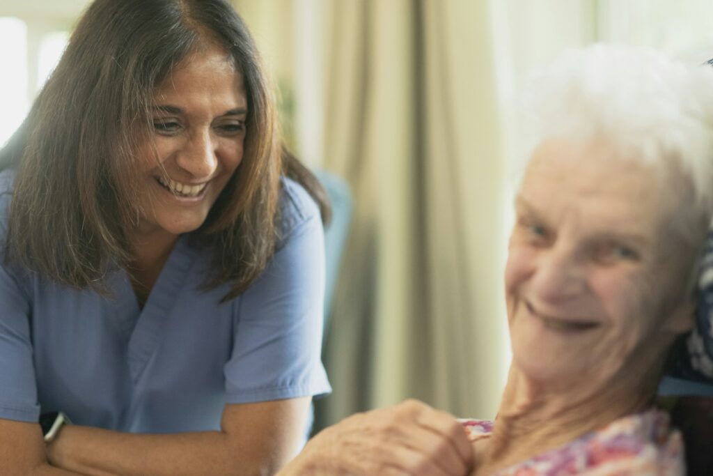 Cuidadora sonriendo junto a una paciente mayor en la habitación