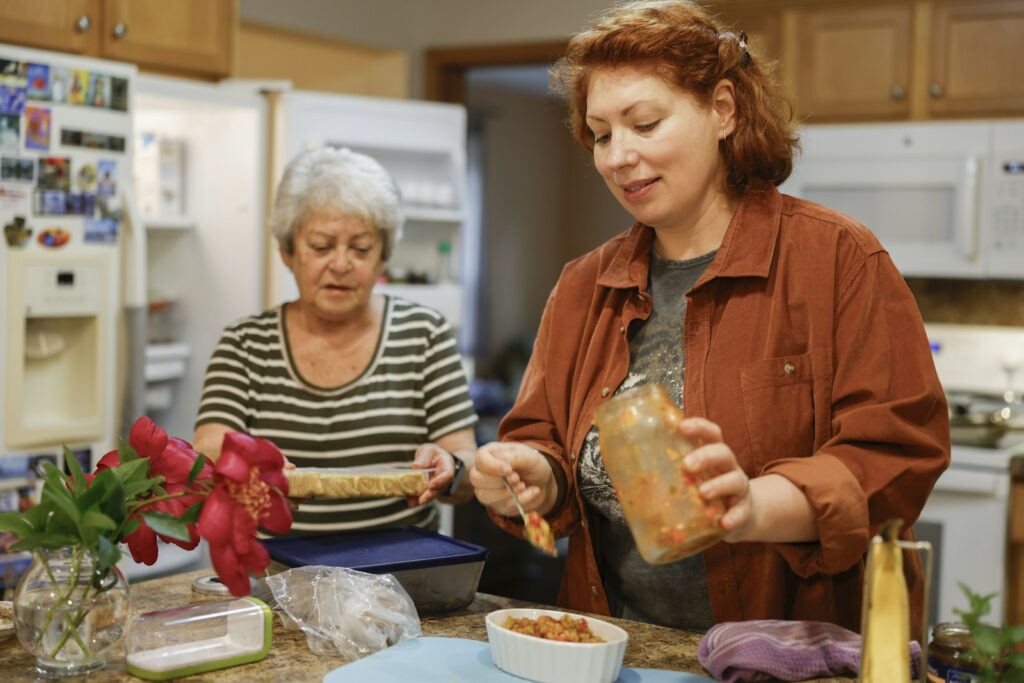 Empleada del hogar cocinando junto a una señora mayor